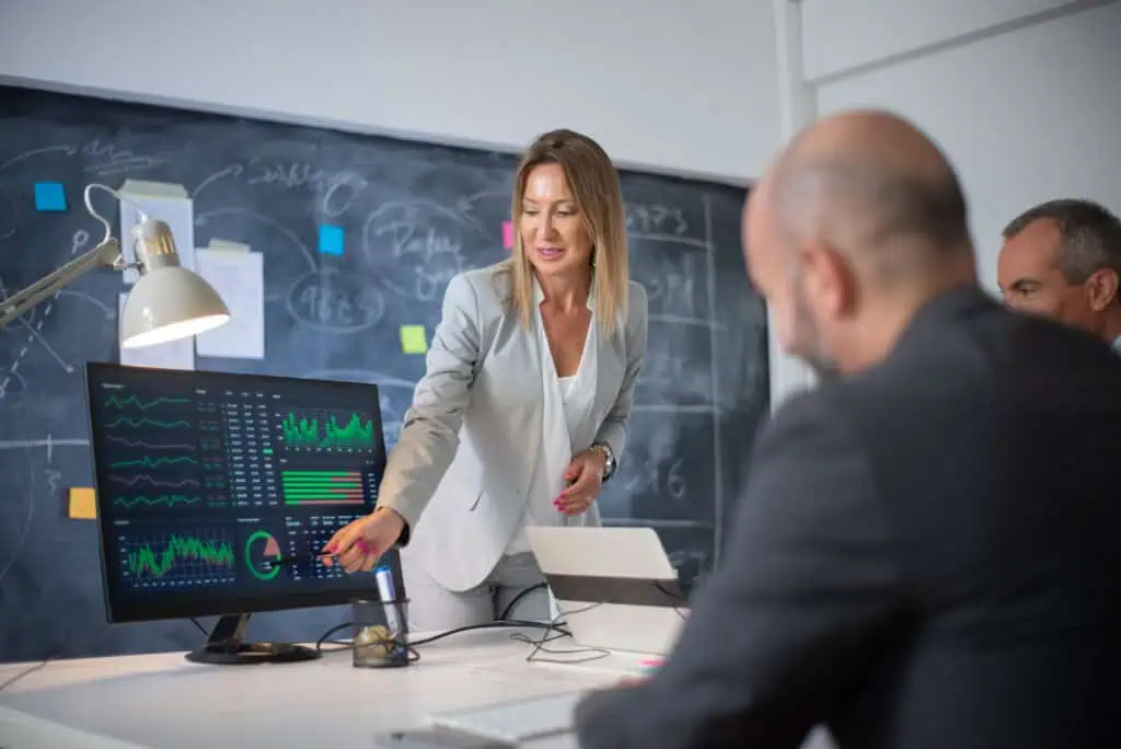 Company employees discussing market data on charts. Skilled woman leader and two men looking at diagrams on computer screen analyzing profit growth.