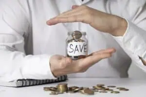 Jar with savings held in a hand with the other hand protecting the top