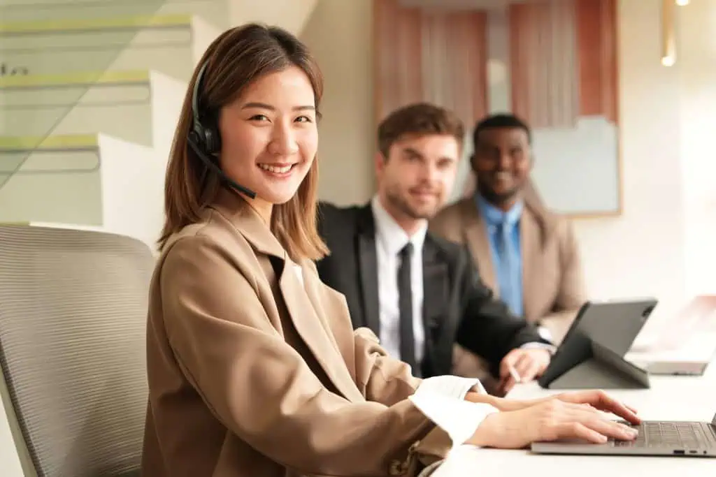 Customer contact team, woman with headset on and two men in the backround, work at an office