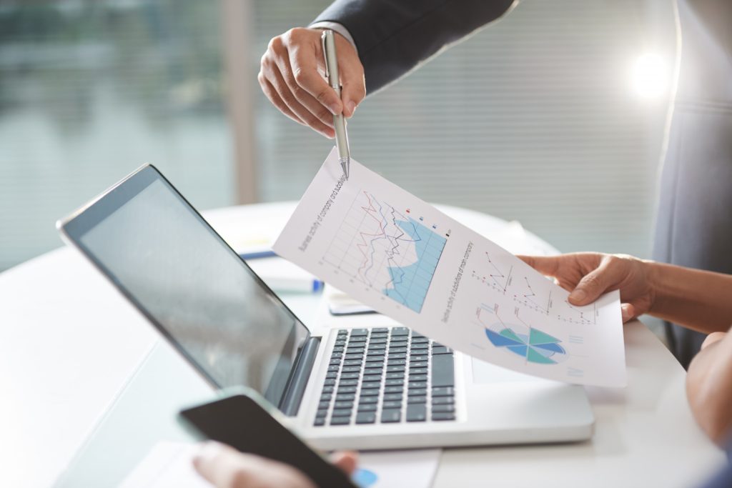 Two coworkers in modern company office are using paper graphs and laptop